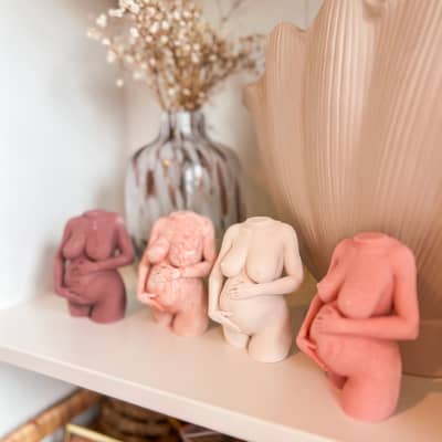 Four statues of pregnant women holding their stomachs, the same design in different colours