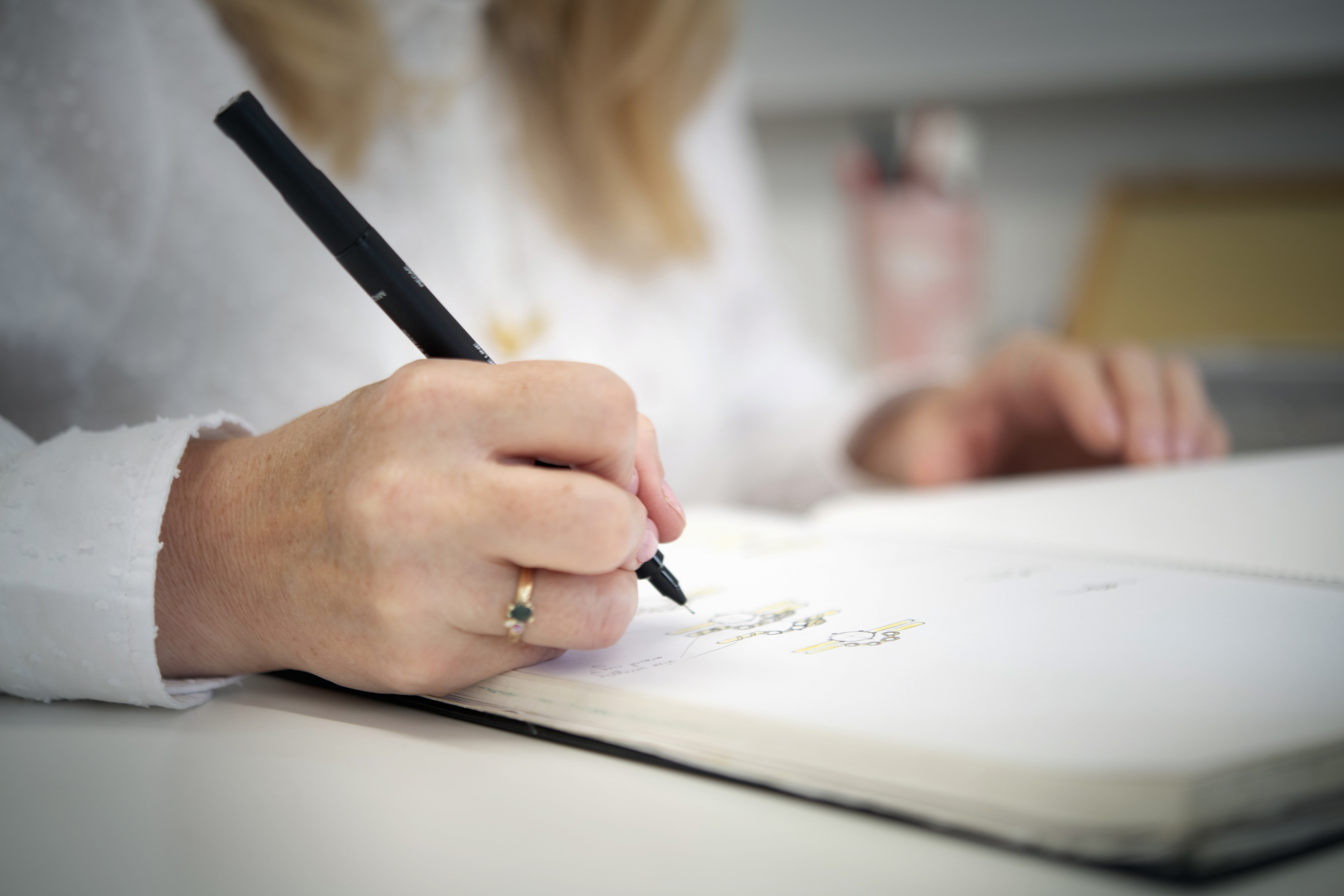Claire Troughton's hand holding a pen and sketching some jewellery designs