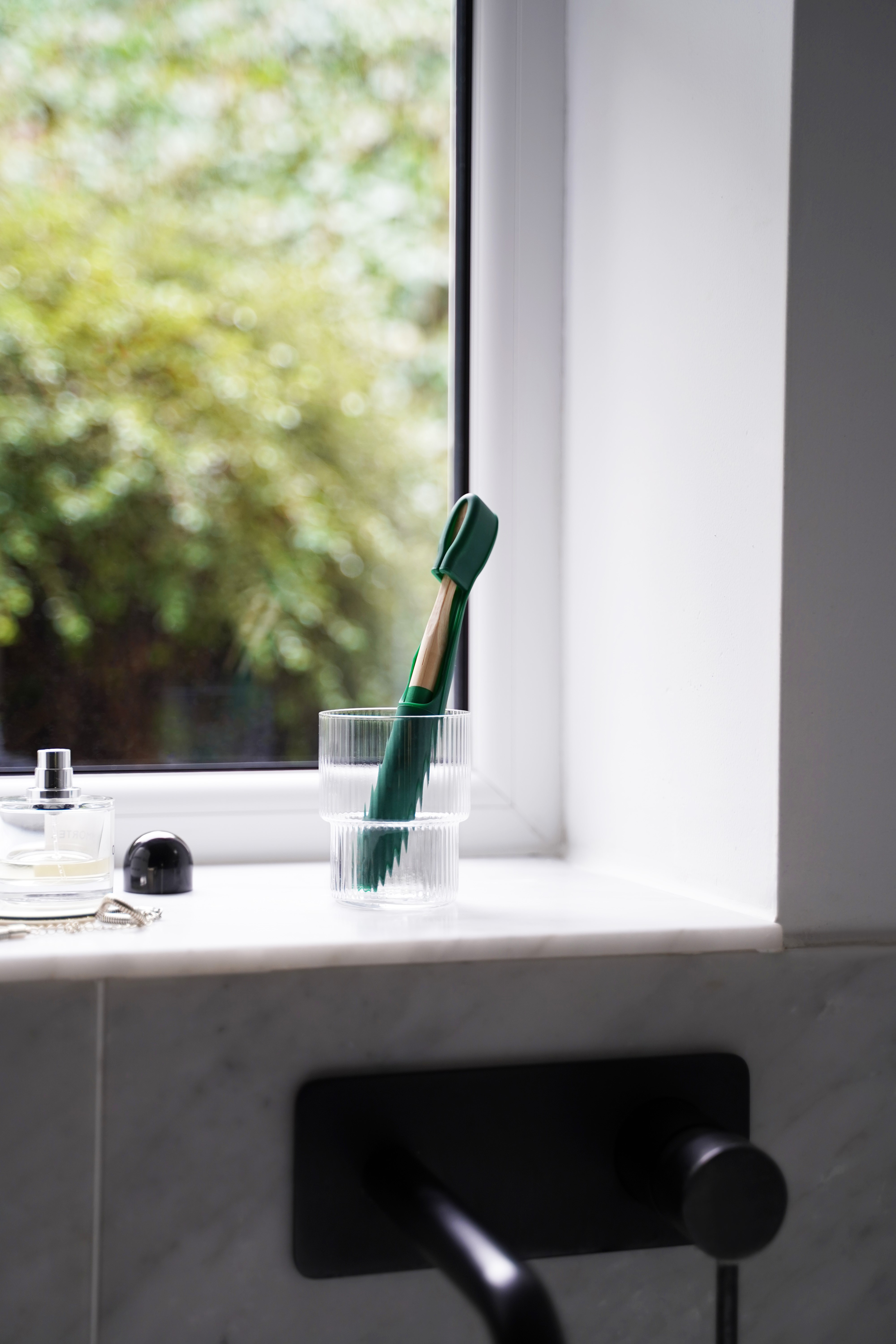 Green Toothbuckle cover and matching bamboo toothbrush in glass bathroom holder on sink 