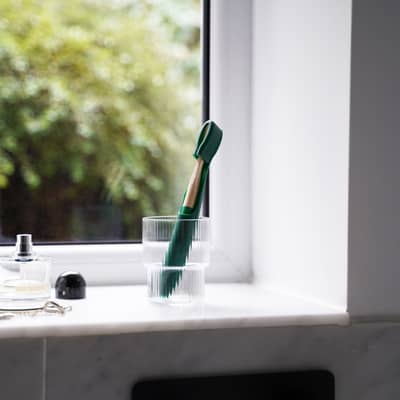 Green Toothbuckle cover and matching bamboo toothbrush in glass bathroom holder on sink
