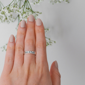 model wear silver ring with the word breathe engraved onto the outside of the band