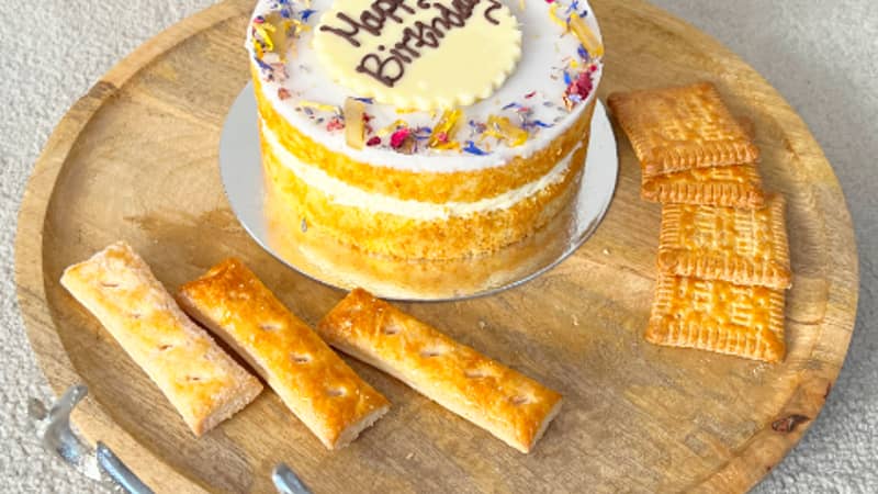 A wooden tray with stag head metal handles laid out with a birthday cake, biscuits and pastries. It is placed beautifully next to a dreamy pampas grass.