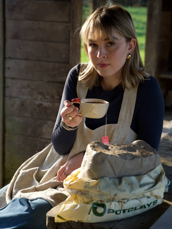 girl holding mug with pottery clay on table