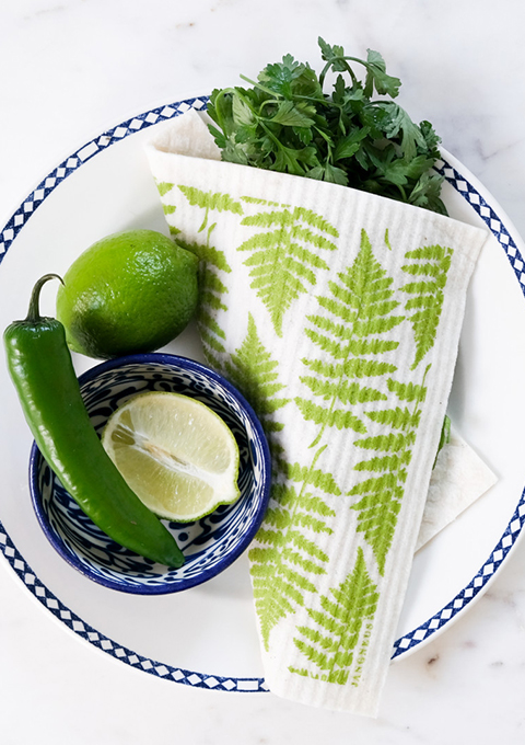 Dishcloth, printed in a green Fern design, wrapped around washed parsley on a plate. 