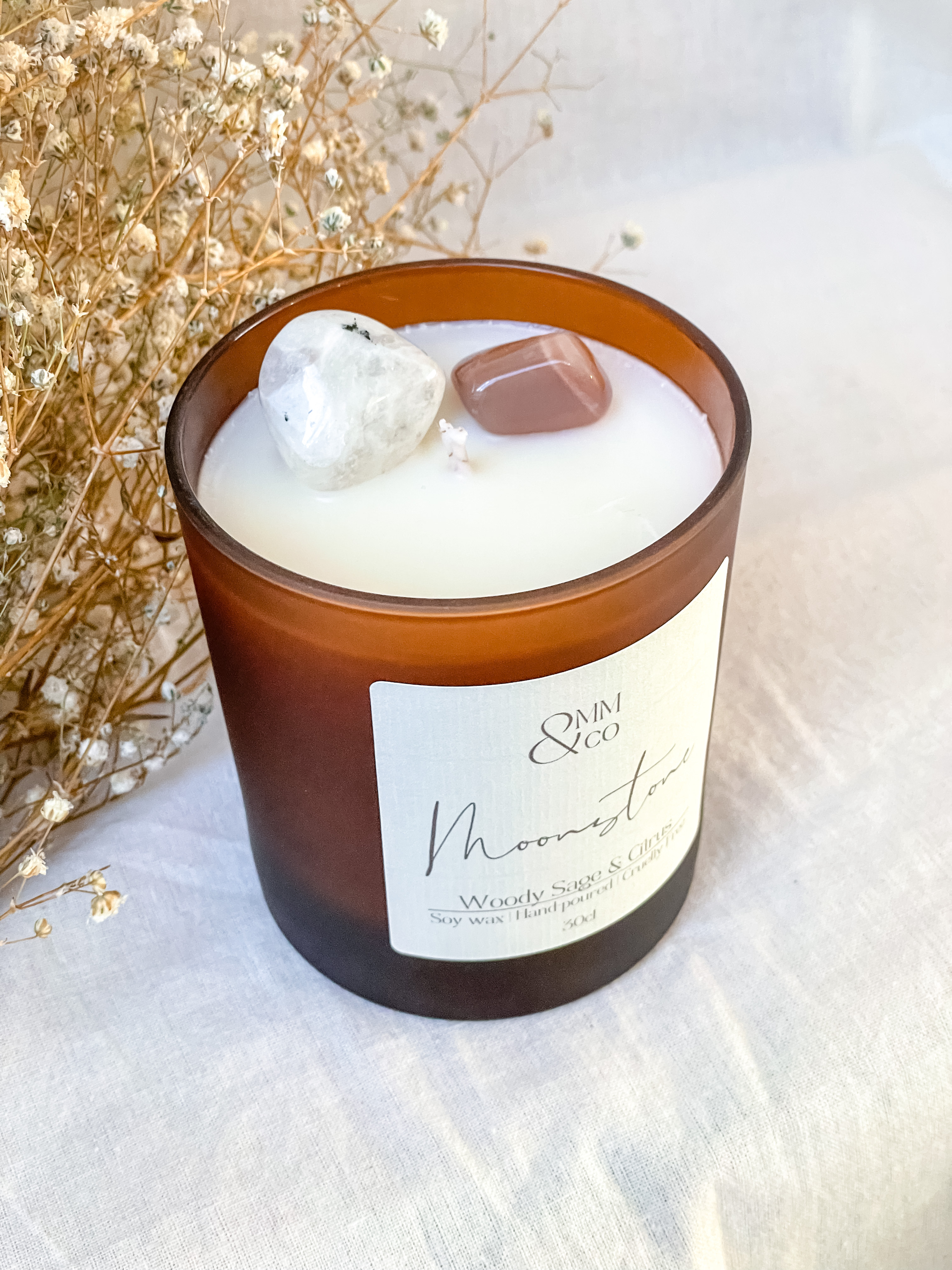 Moonstone crystal candle. A frosted amber jar, with 2 Moonstone crystals infused in the wax. Dried florals in the background.