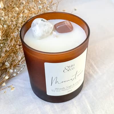 Moonstone crystal candle. A frosted amber jar, with 2 Moonstone crystals infused in the wax. Dried florals in the background.