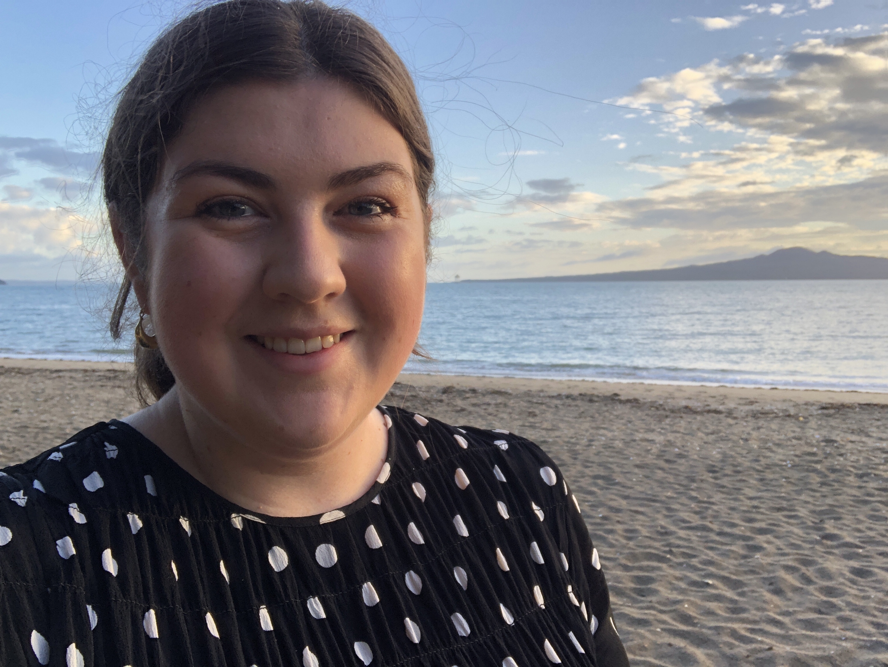 Woman standing on a beach with a cloudy blue sky in the background.
