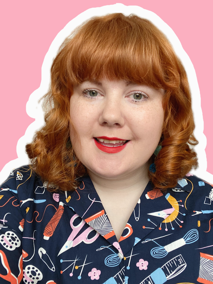 White woman wearing rainbow pom pom headband and holding a cup of coffee in her craft room