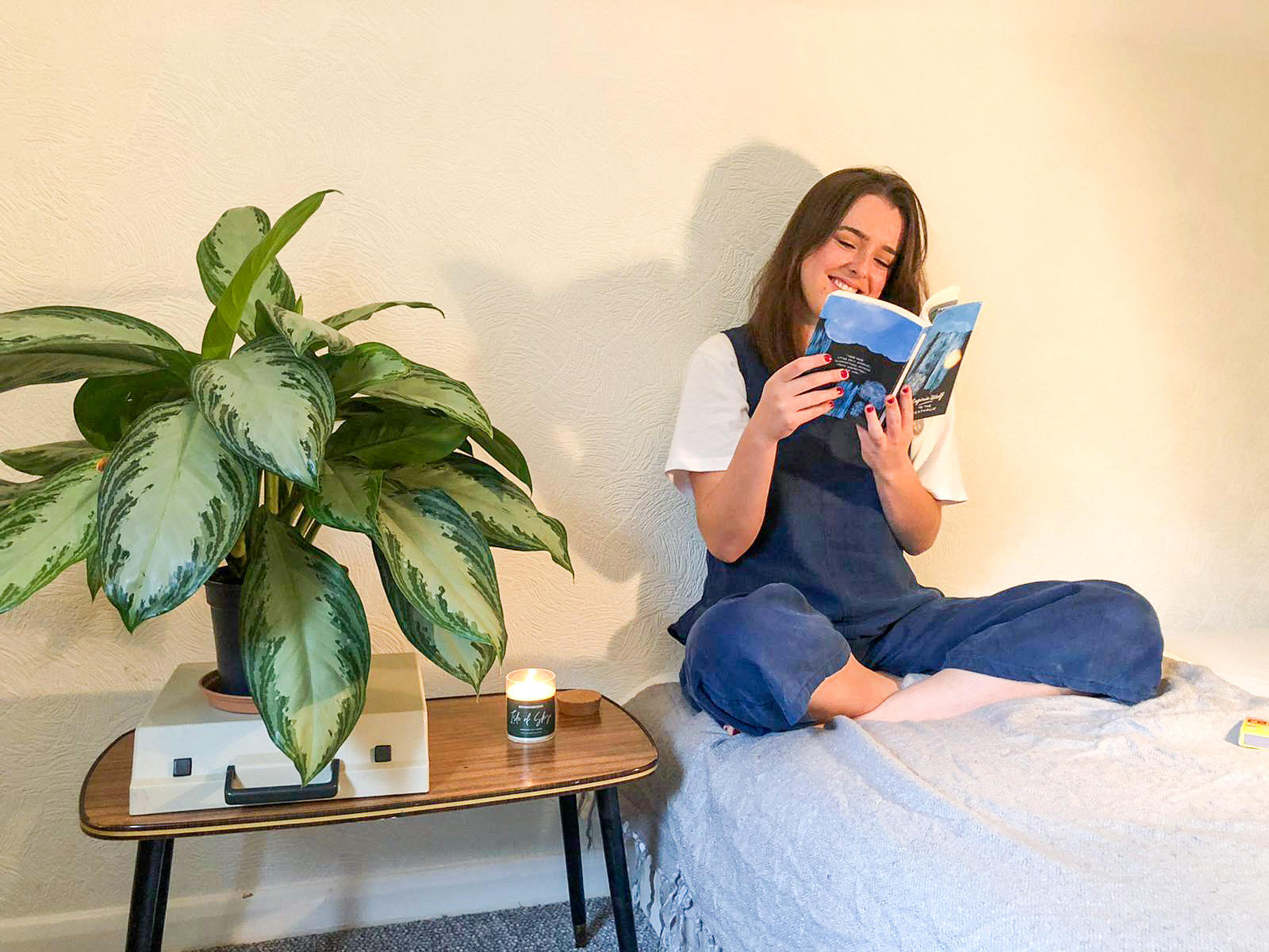 A woman reading To The Lighthouse with the Isle of Skye candle lit on the side table. 