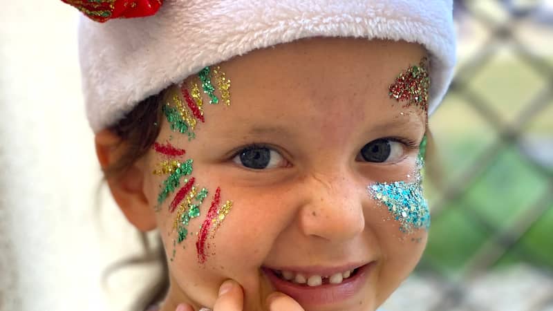 a little girl with a Santa hat holding a Christmas bauble with eco glitter on her face