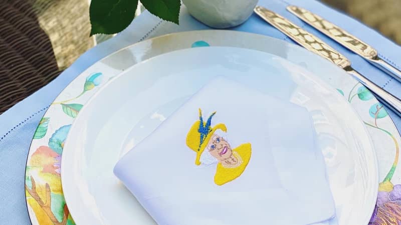 White linen hemstitch napkin with an embroidered image of Her Majesty the Queen
