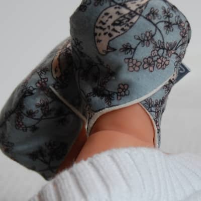 baby feet wearing a pair of slippers in blue-grey recycled fabric with a bird and flower print