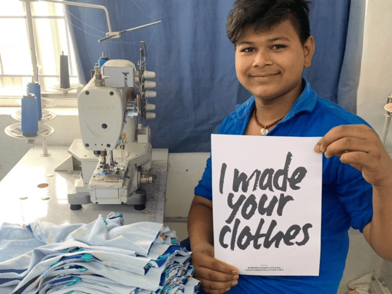 Image of a man holding a sign saying 'I made your clothes'