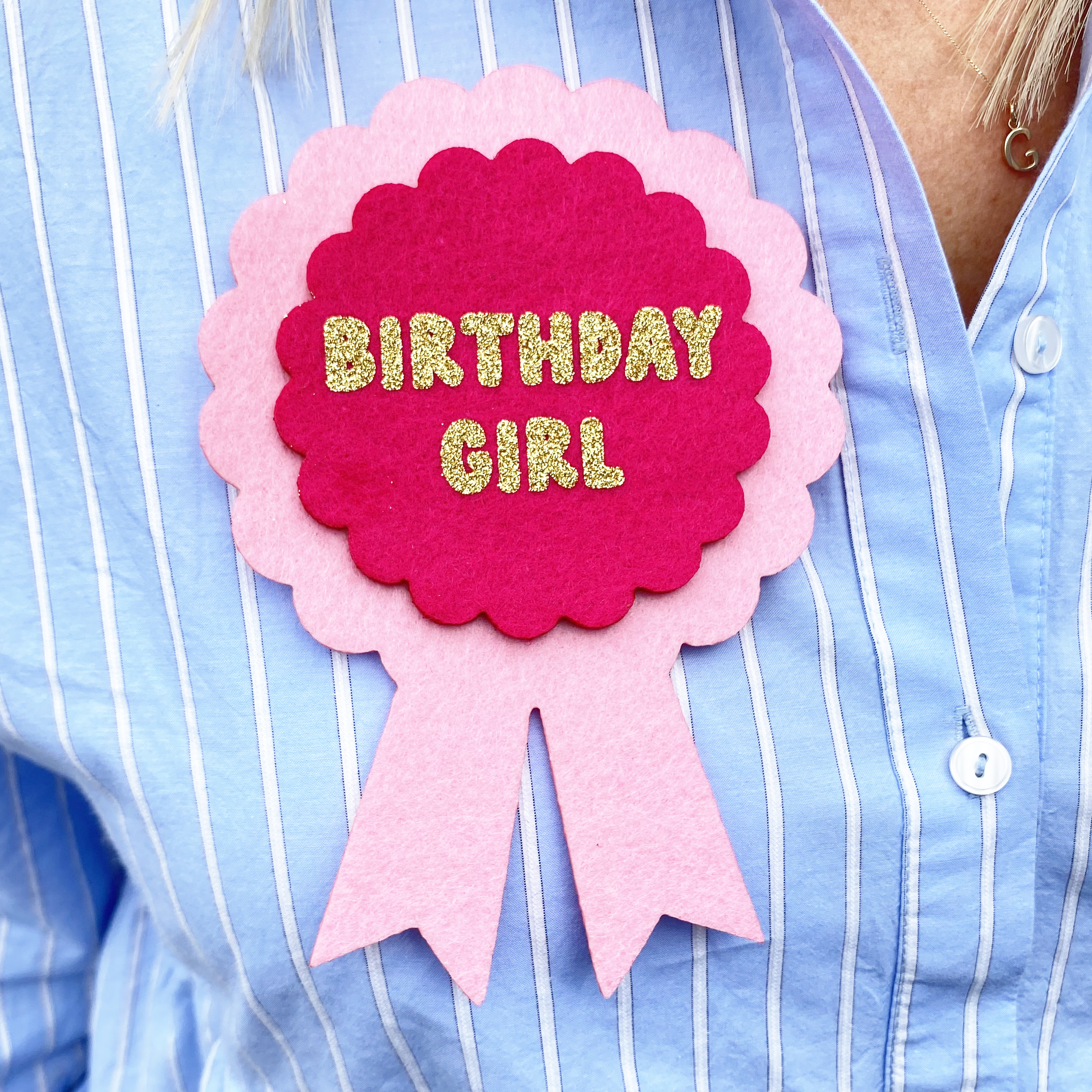A pink oversized birthday badge witht he words BIRTHDAY GIRL in gold glitter