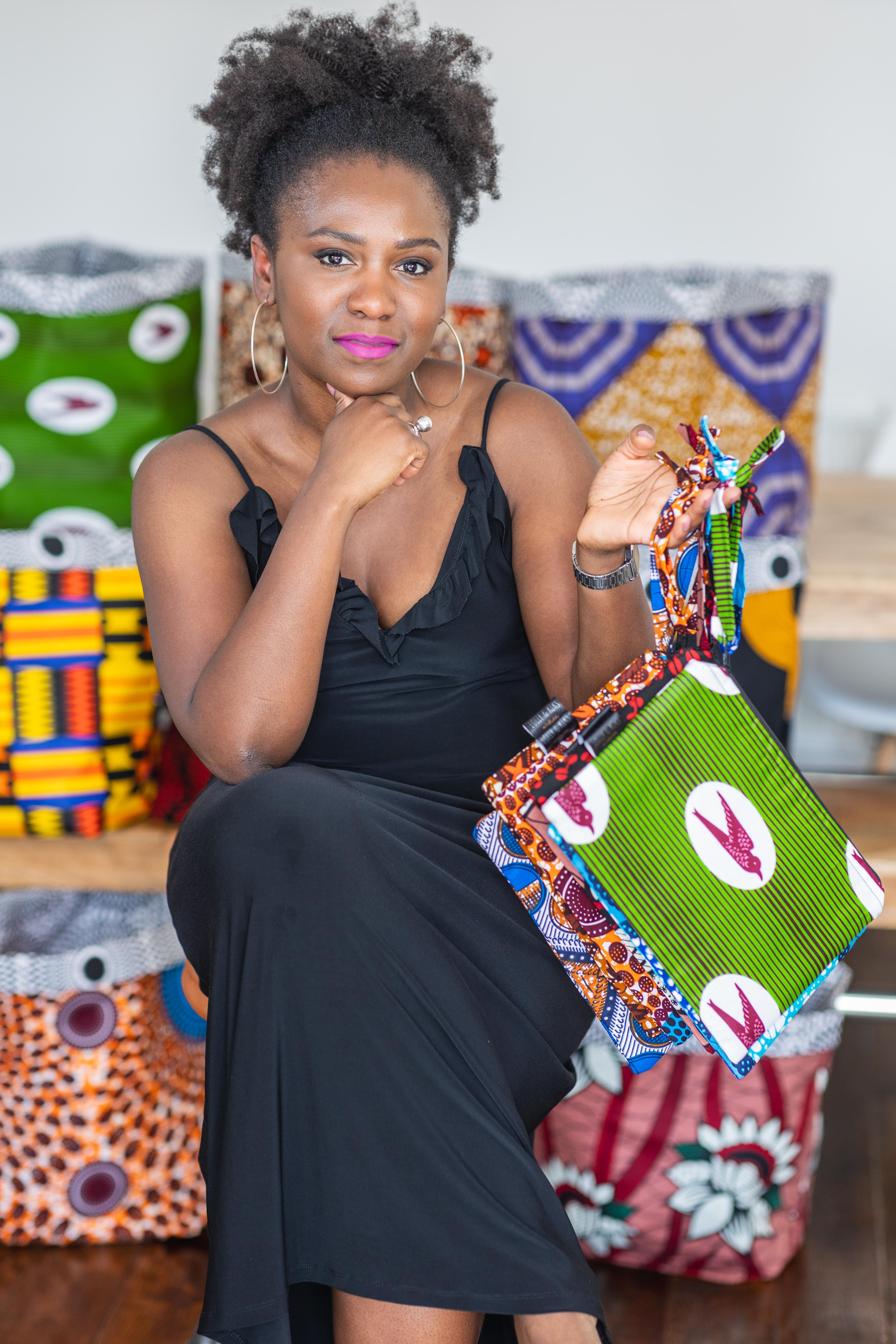 Black woman holding afrcian print pouch bags in front of colourful african wax print baskets