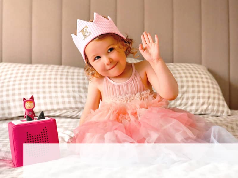 A happy child dressed as a princess, with a custom crown, in a magical moment, celebrating her bespoke music song on her Tonies player, designed just for her.