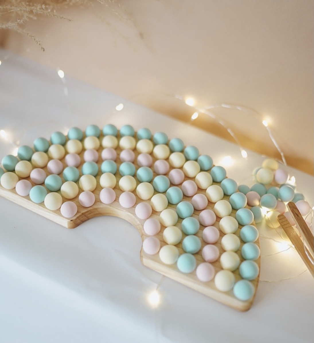 wooden rainbow shape filled with pastel pom poms