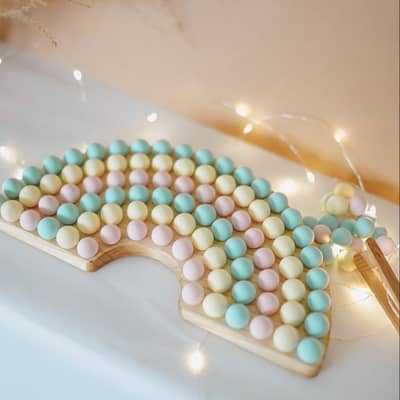 wooden rainbow shape filled with pastel pom poms