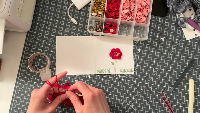 An image of Njomza, co-founder of Nyoki Handmade, crafting crochet flowers with organic yarn to embellish birthday cards.