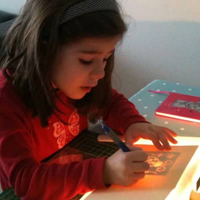 An image of a founder's daughter, as a young child, learning the craft of embossing a greeting card.