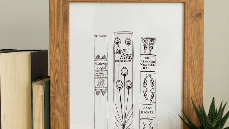 A framed print of a black and white illustration of three book spines by Georgina The Librarian
