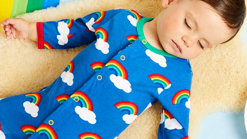 A sleeping baby wearing a Toby Tiger Organic Rainbow Print Babygrow