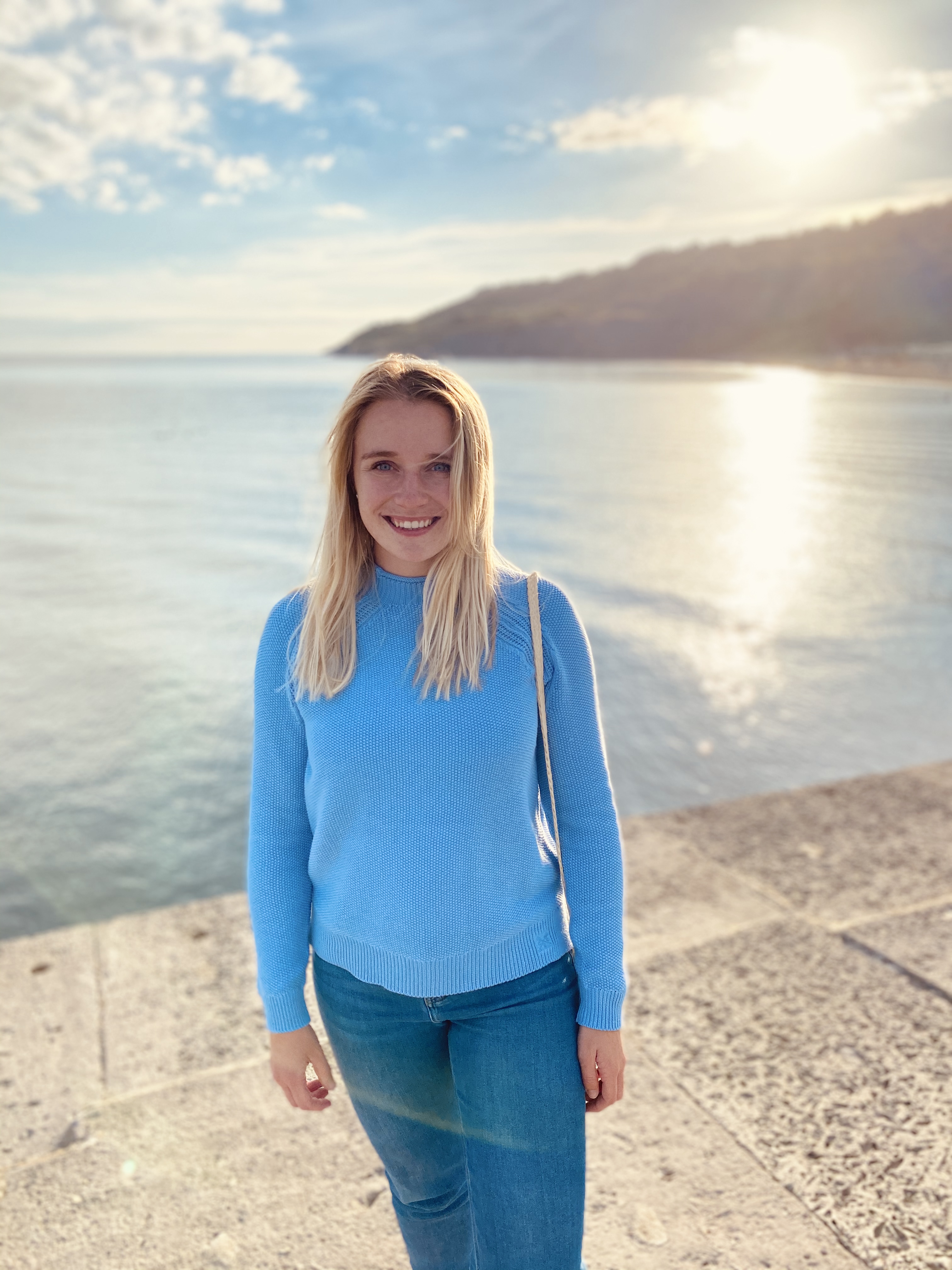 Woman standing on beachfront. Blue jumper and jeans