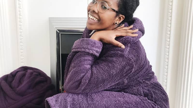 Nadine sitting on the fireplace in her dressing gown with a big ball of wool