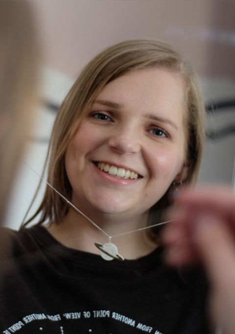 white woman holding up saturn planet necklace and wearing earth blue earrings