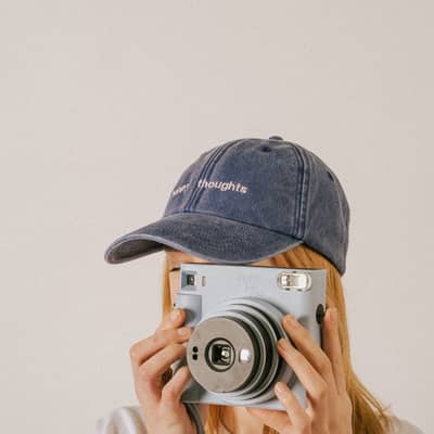 Girl in embroidered cap that says Happy thoughts taking picture with polaroid camera