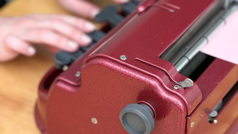 A close up of a red coloured Perkins brailler, with hands on the keys