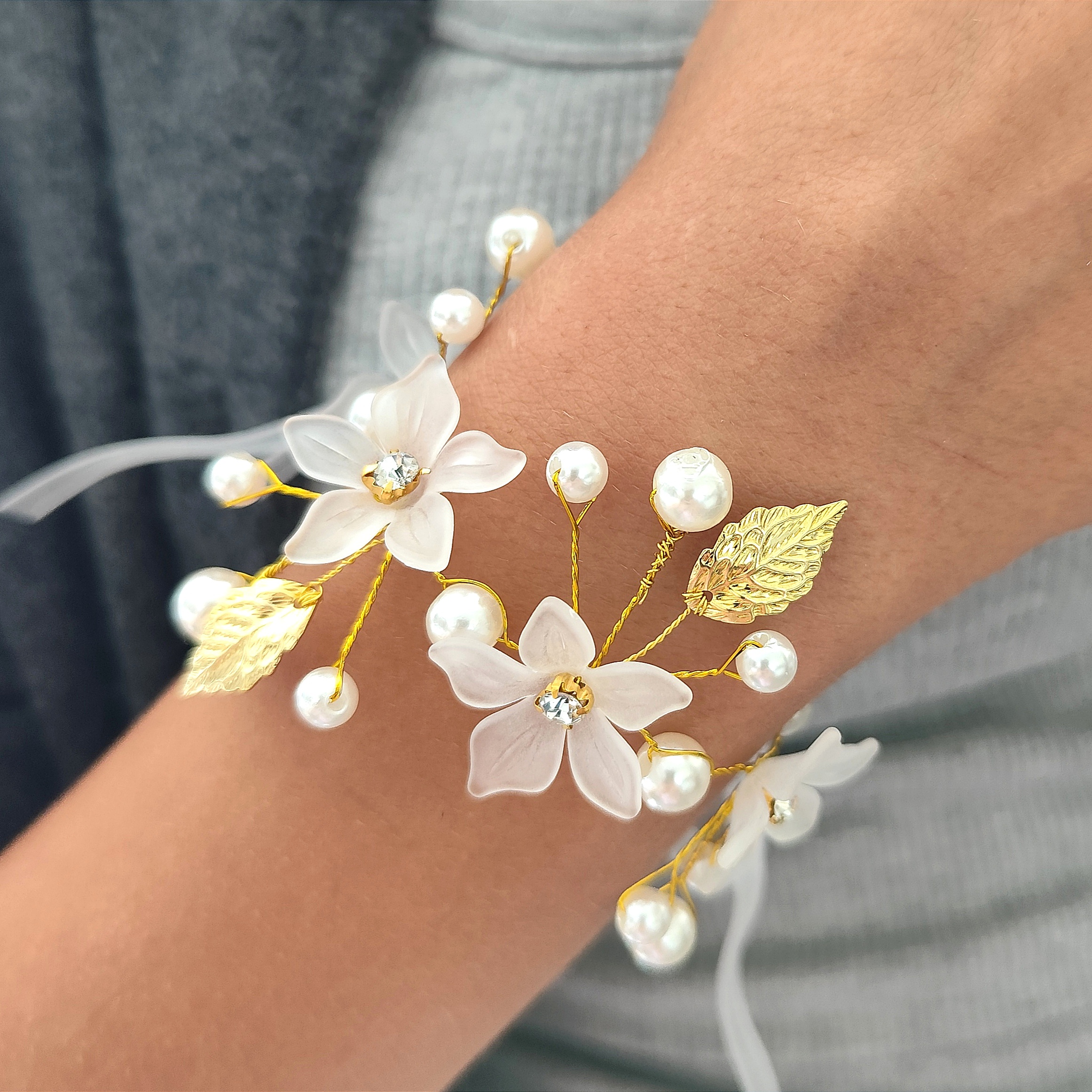 This is a beautiful and intricate wedding corsage. The corsage features delicate white flowers adorned with golden leaves and pearls, all connected by slender g