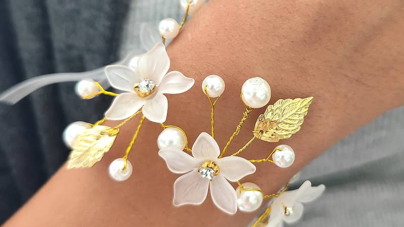 This is a beautiful and intricate wedding corsage. The corsage features delicate white flowers adorned with golden leaves and pearls, all connected by slender g