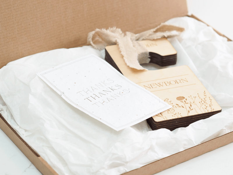 Wooden engraved wardrobe dividers tied together with natural linen ribbon, resting on white tissue paper next to a seeded paper thank you card