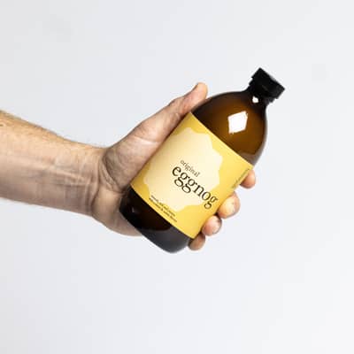 honestyolk eggnog bottle next to a glass of eggnog sprinkled with grated nutmeg