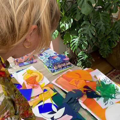 Image of Charlotte working on a collage on her desk with lots of colourful pieces of paper.