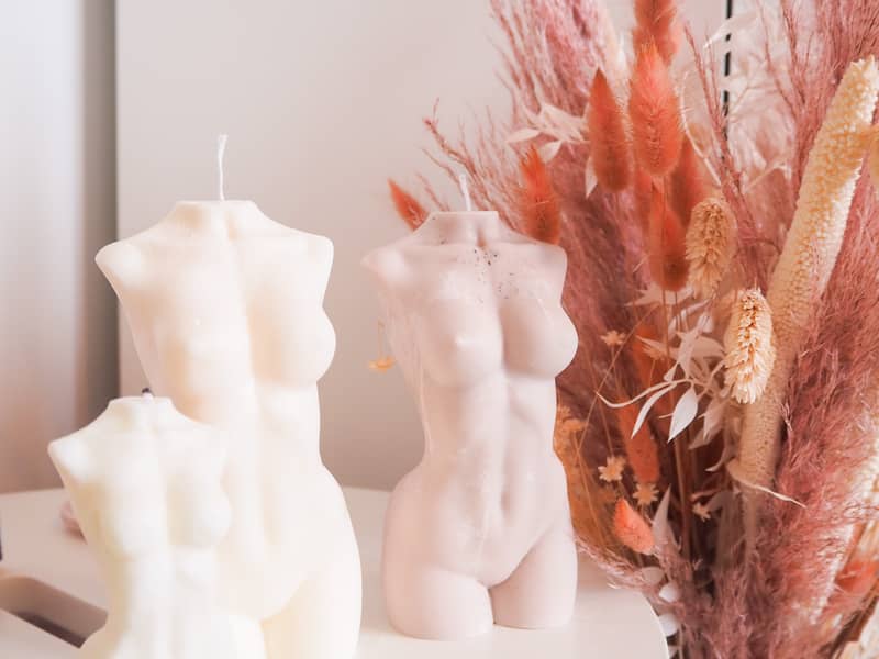 Two large Grand Grace candles next to a smaller one, stood on a table with a dried flower display in the background