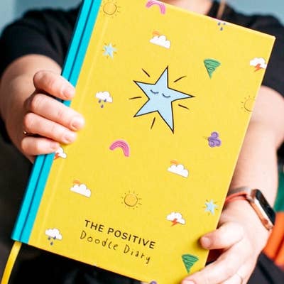 The yellow and turquoise Positive Doodle Diary being held towards the camera
