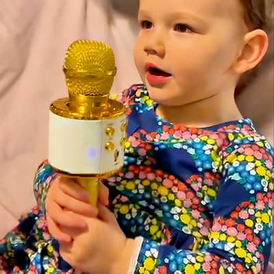 A happy child in a magical moment, celebrating her bespoke music birthday song designed just for her, singing into a golden microphone