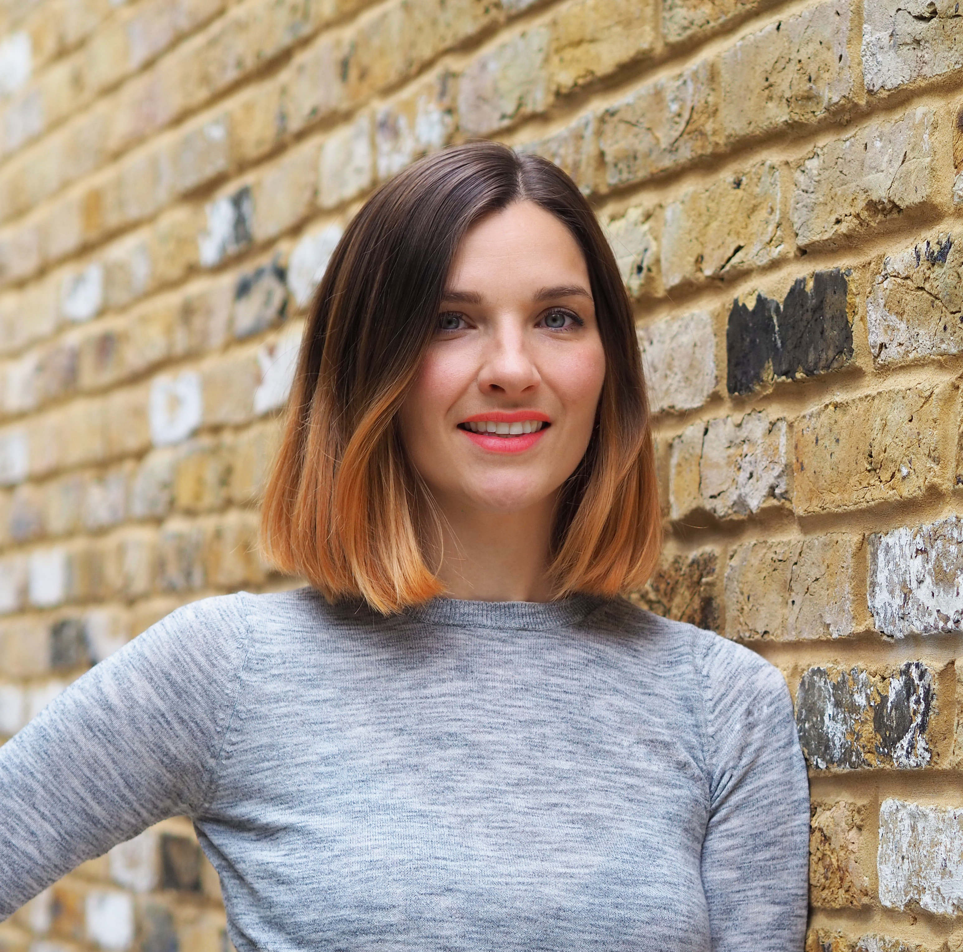 A woman with brown hair standing by a wall