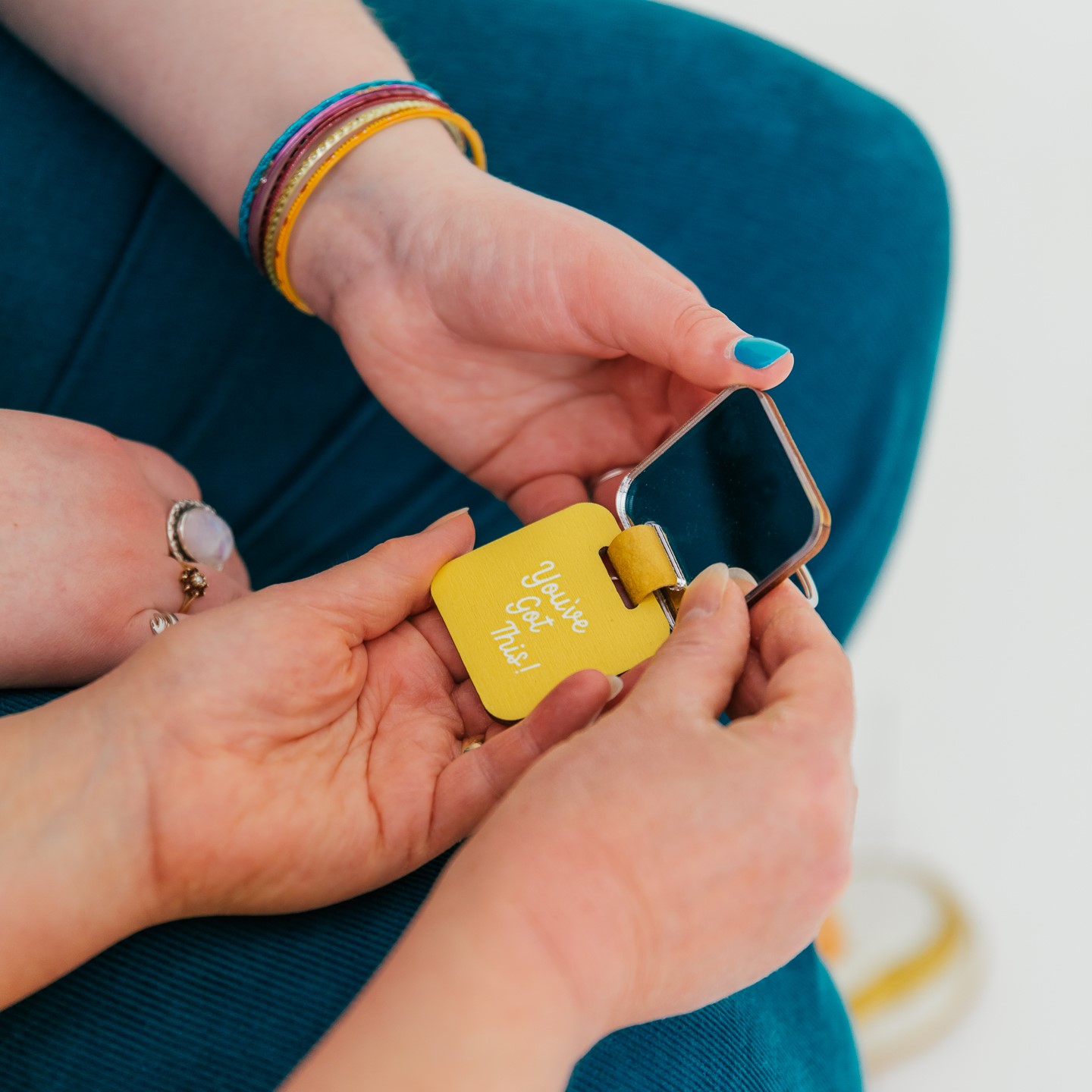  A person handing another person in teal trousers a keyring with a motivational message and mirror
