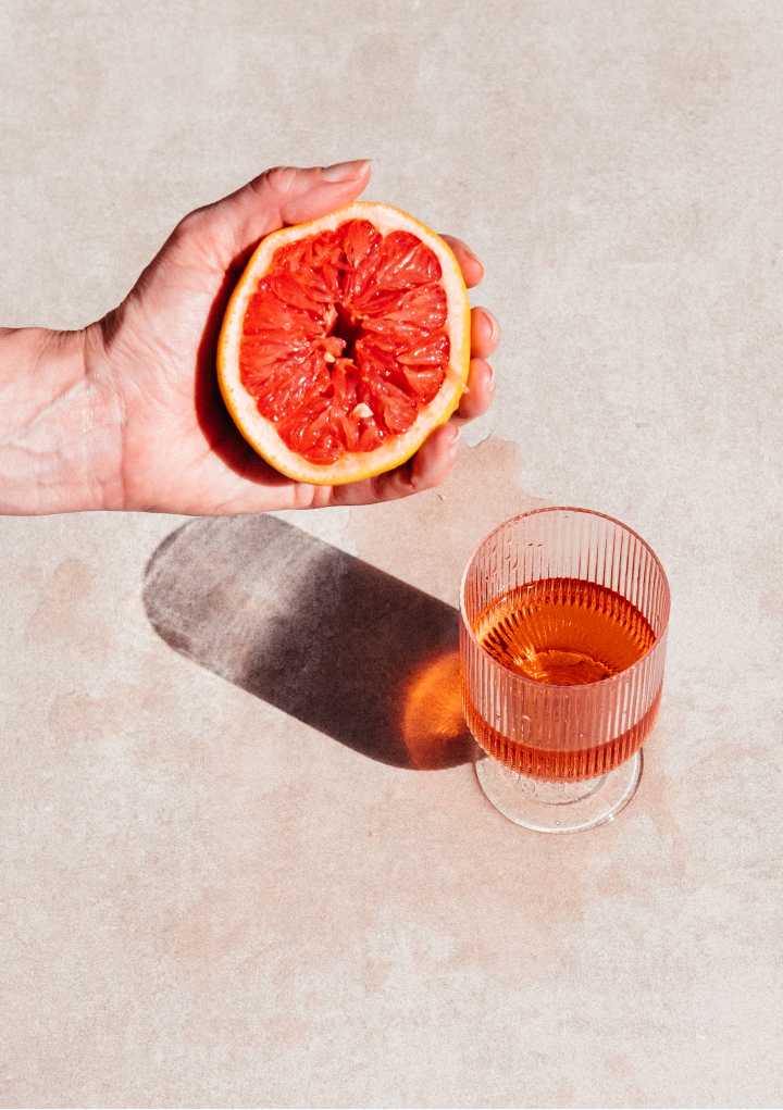 Hand crushing a grapefruit next to a glass of DEFY rosé wine