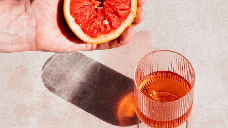 Hand crushing a grapefruit next to a glass of DEFY rosé wine
