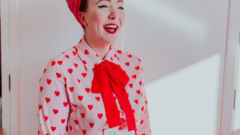 Ellie, owner of Dottie's Paper Co. is dressed is a vintage style outfit with a pink and red heart blouse, red swing skirt and hair done up in a beehive.