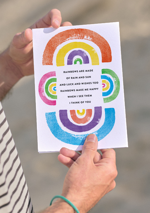 Two hands holding a poem about friendship surrounded by rainbows