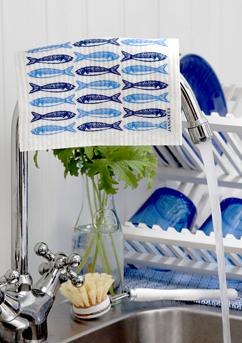 Dishcloth, screen printed with a blue sardines design, hanging over a kitchen tap.