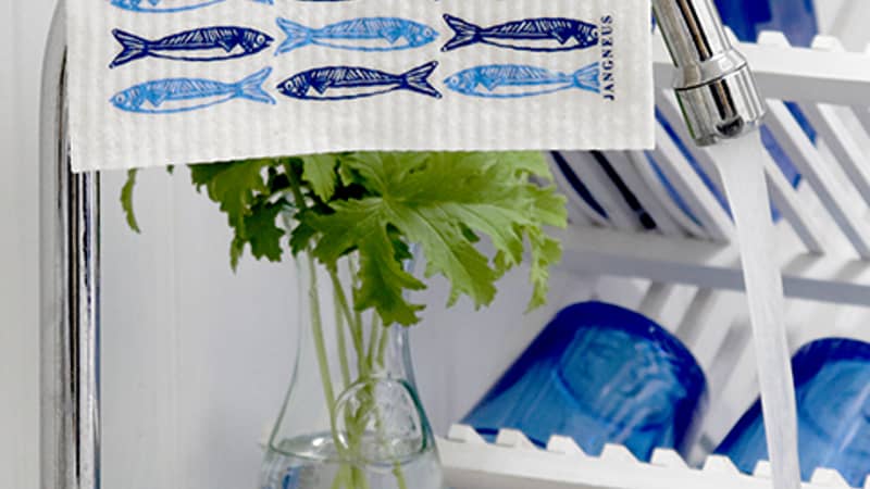 Dishcloth, screen printed with a blue sardines design, hanging over a kitchen tap.