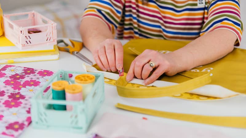 lady in a stripy top and head hairband pinning together a mustard coloured tote bag