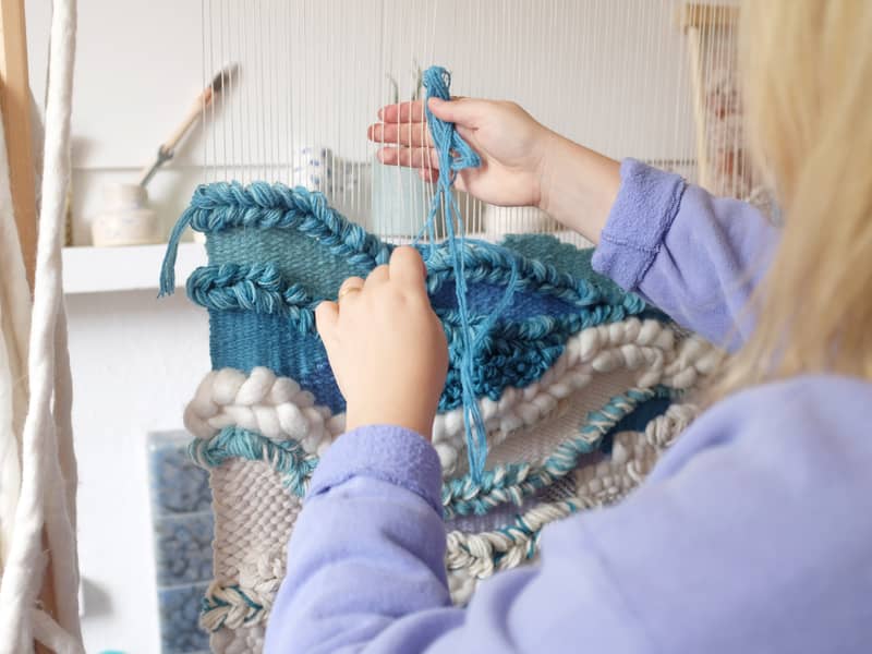 Lucy Rowan weaving a large blue weaving on a wooden loom