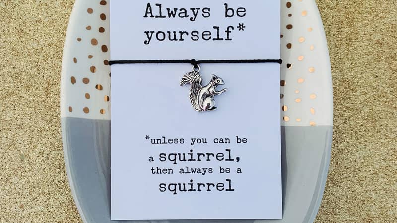 black cord wish bracelet mounted on white card, text reads always be yourself, unless you can be a squirrel, then always be a squirrel